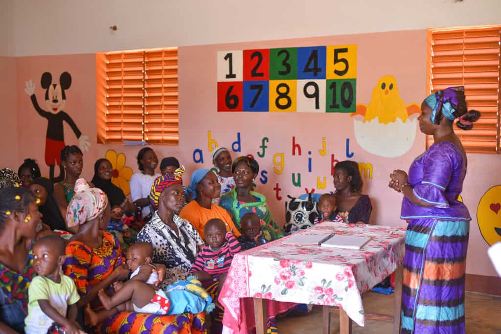 Woman talking with a group of mothers with young children in a children's classroom.