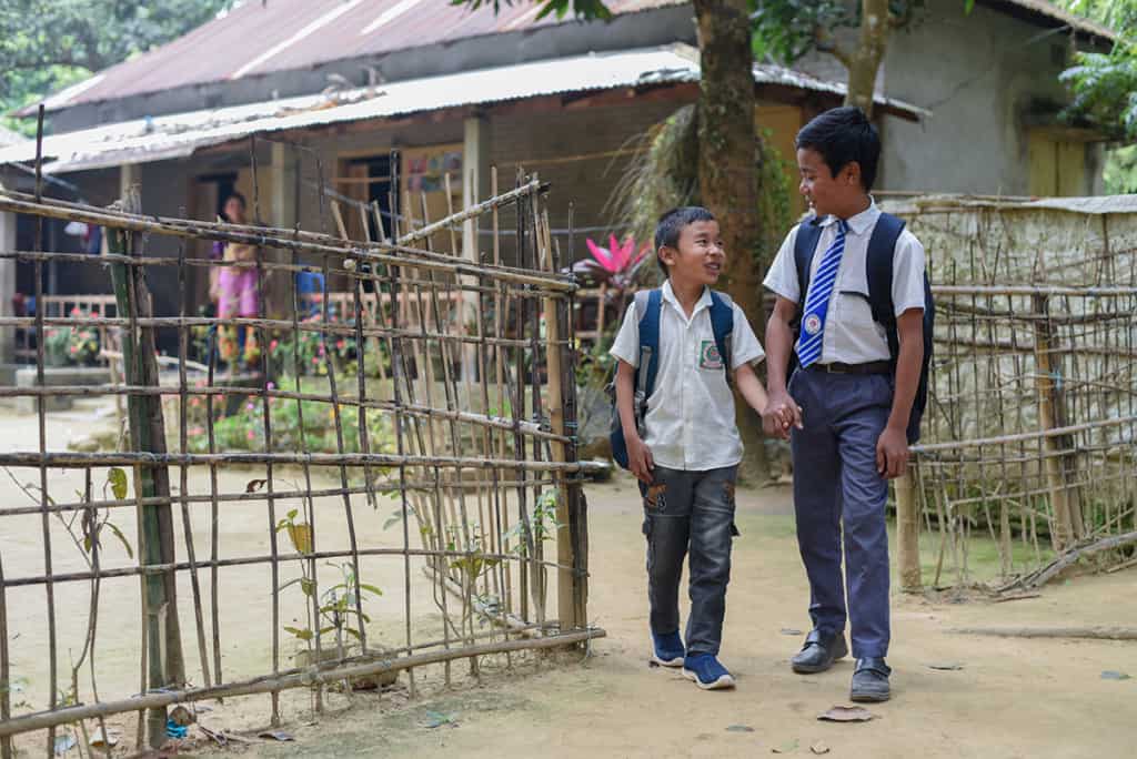 Two boys walk out of a fence. They are wearing white shirts and backpacks, ready for school