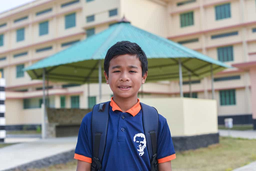 a boy wearing a blue and orange shirt smiles at the camera.