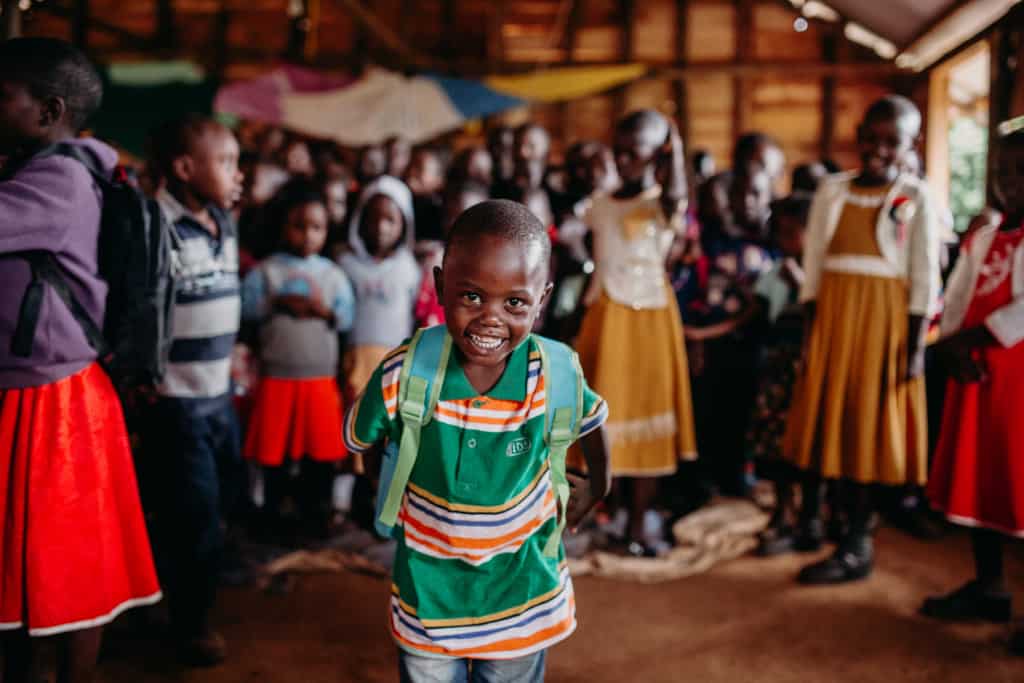 A young boy smiles while wearing a new backpack he got at a Compassion Christmas celebration. Children are standing behind him