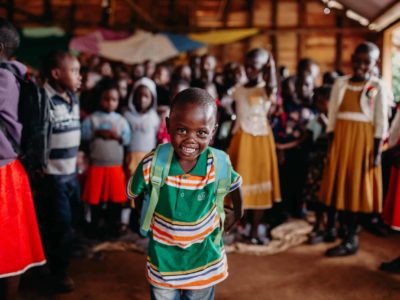 A young boy smiles while wearing a new backpack he got at a Compassion Christmas celebration. Children are standing behind him