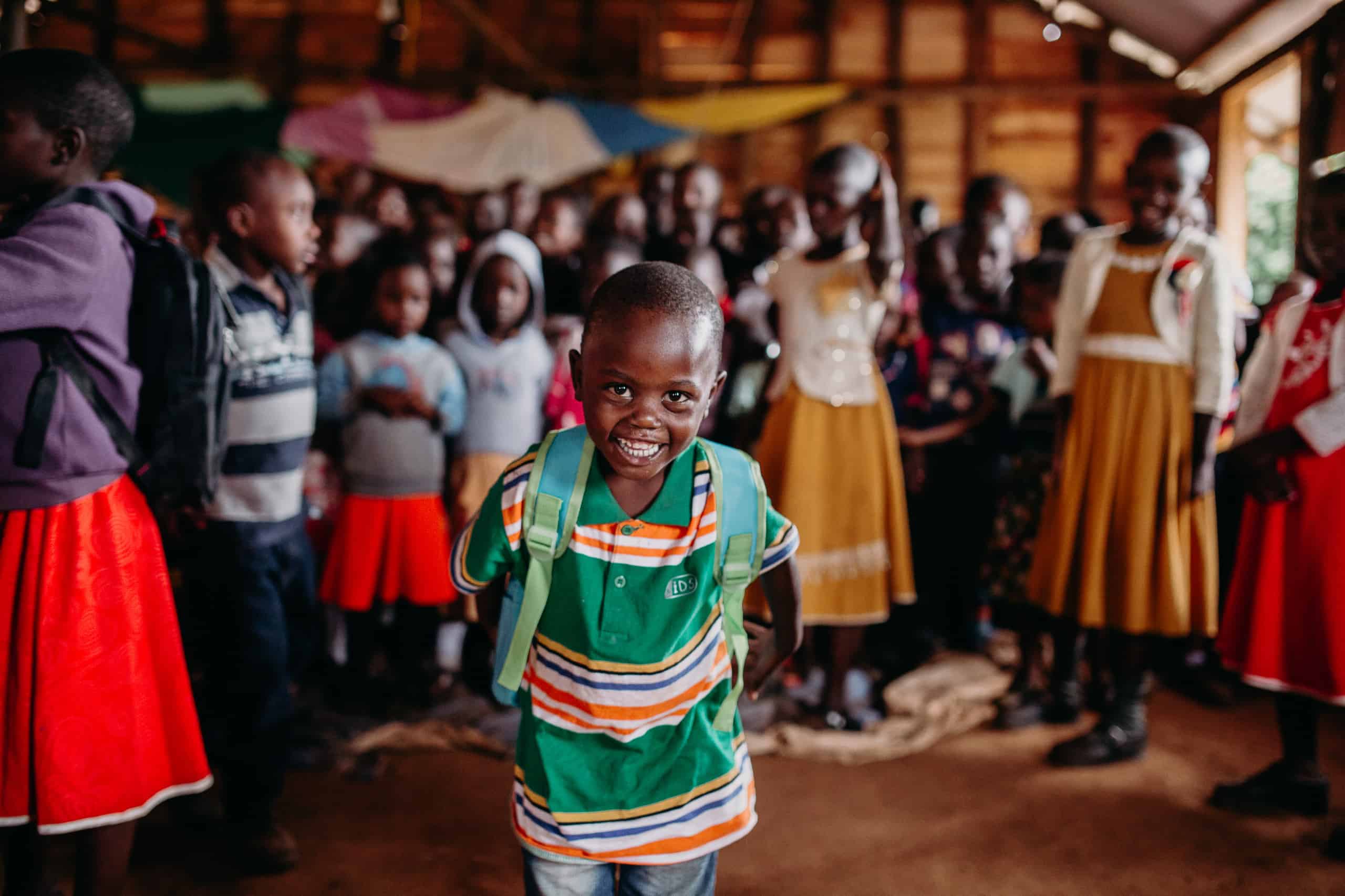 A young boy smiles while wearing a new backpack he got at a Compassion Christmas celebration. Children are standing behind him