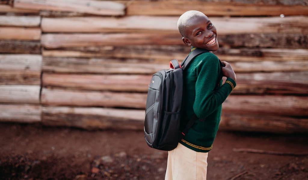a girl wearing a green sweater smiles while wearing the new backpack she got at the Compassion Christmas celebration