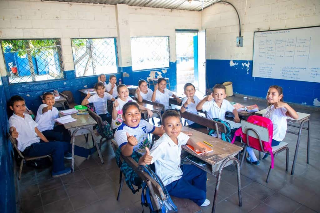 Students in El Salvador give thumbs up signs from their school classroom
