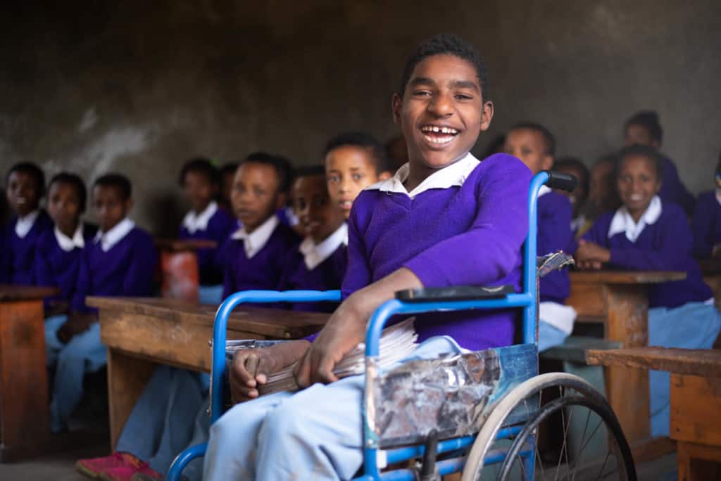 Eyuael is pictured here at the project with a large group of other boys. They are all wearing the project's uniform, light blue pants and a purple sweater. Eyuael is smiling at the camera.