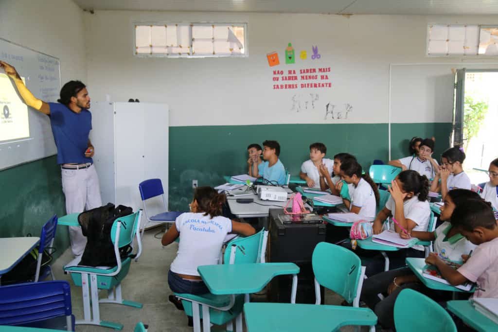 A teacher wearing a blue shirt and white pants presents a lessons in a special classroom for watching a video.