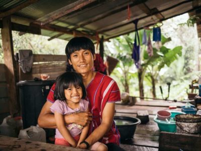 A smiling father in Thailand puts a protective arm around his young daughter, who is wearing a pink shirt and smiling