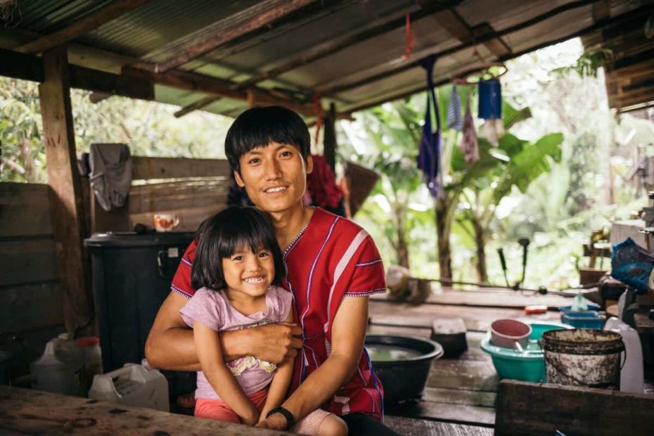 A smiling father in Thailand puts a protective arm around his young daughter, who is wearing a pink shirt and smiling