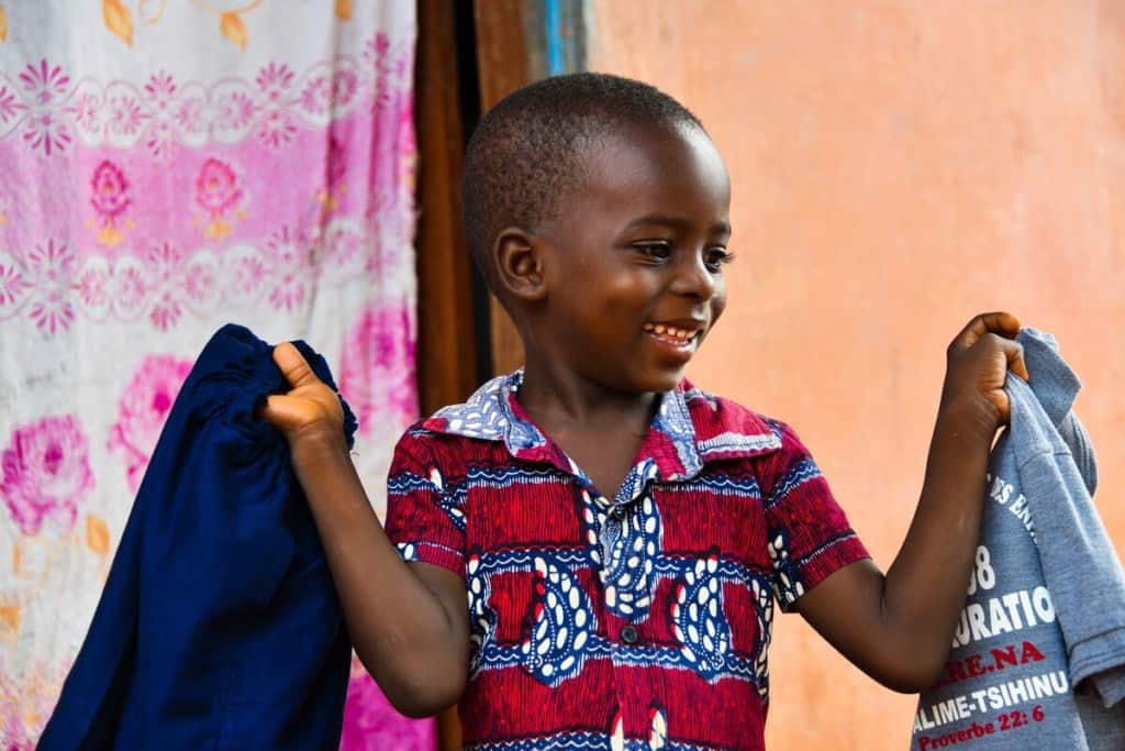 A young boy in Togo holds up a new pair of blue pants and a shirt