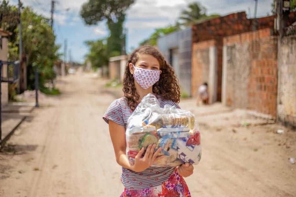 A teenage girl holds a packet of supplies she received from her Compassion center. She is wearing a face mask 
