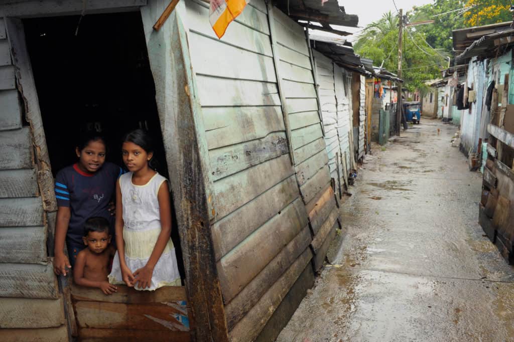 Three Sri Lankan children in a home, with a view from an alley.