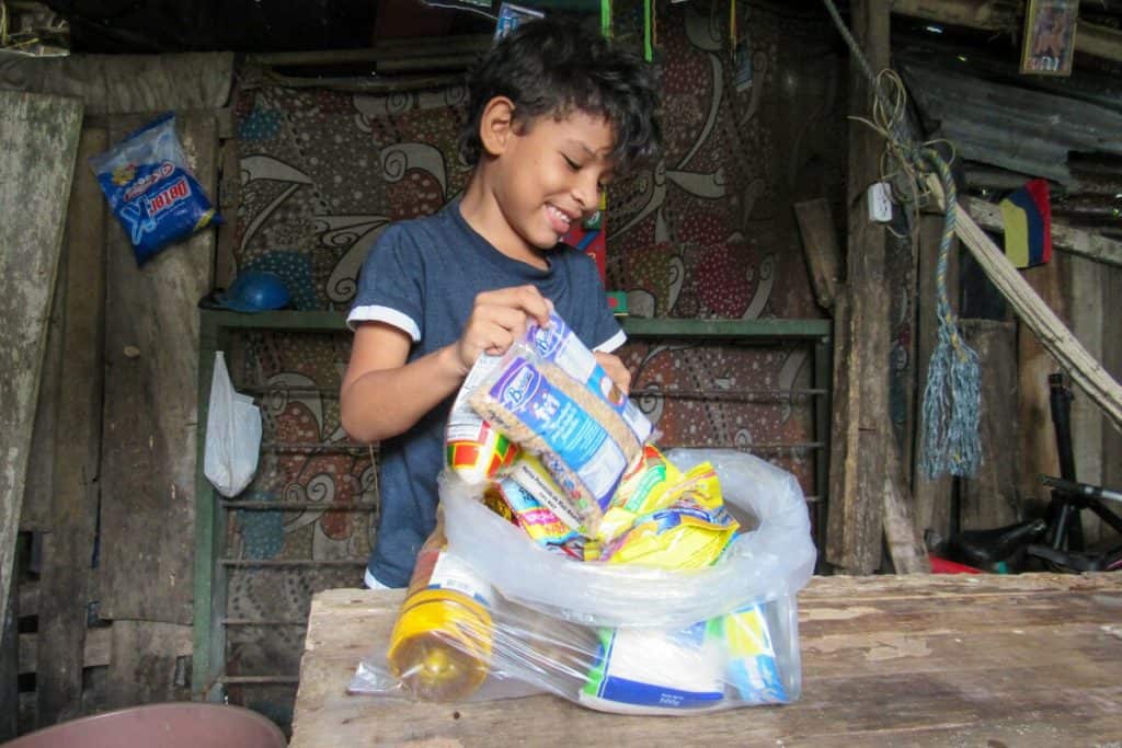 A boy smiles as he looks through a plastic bag filled with food staples