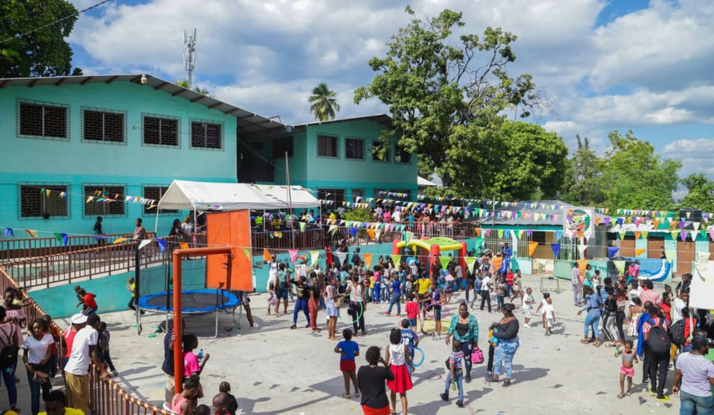 A large group of people participating in the Fun Fair Day at the Compassion project. They are all in the courtyard in front of a green building.