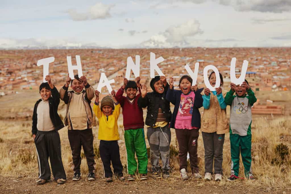 Eight children stand on a hill above a city holding up white letters that say THANK YOU.