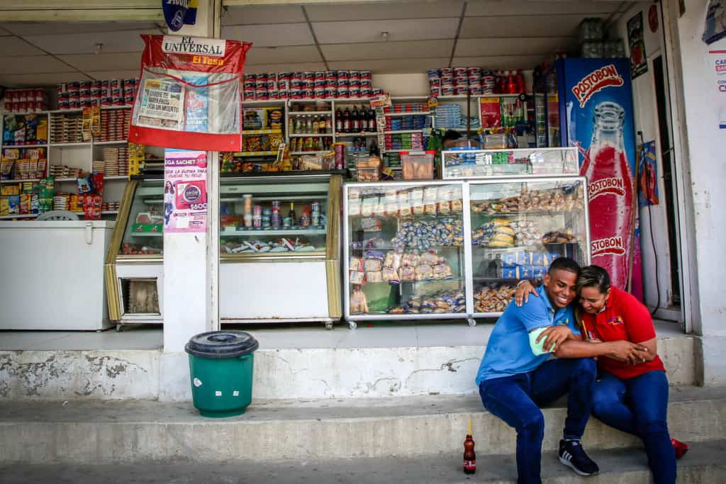 Francisco, in blue, and Enith, in red, sit on the steps outside a store. They are smiling and have their arms around each other, hugging.