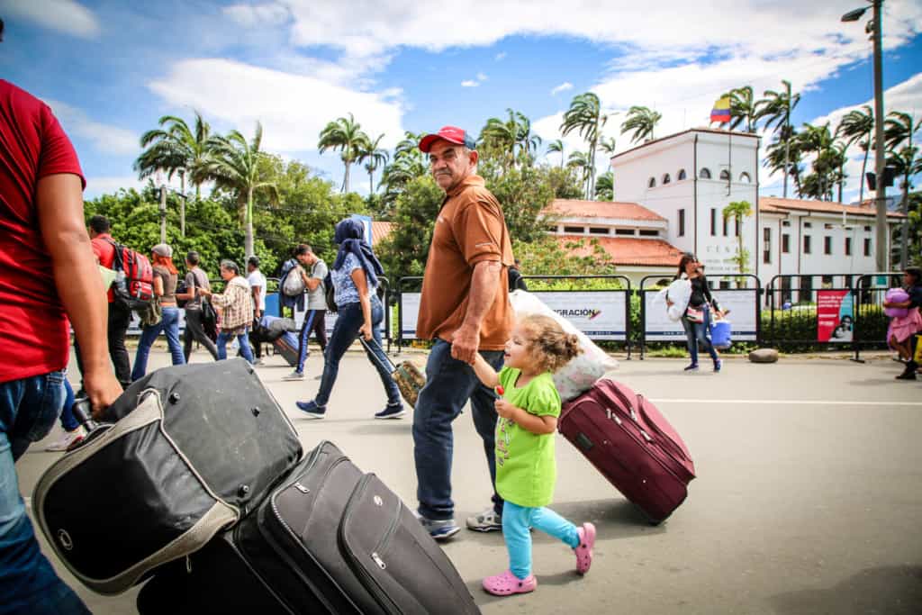 An older man holding the hand of a little girl while pulling a suitcase.