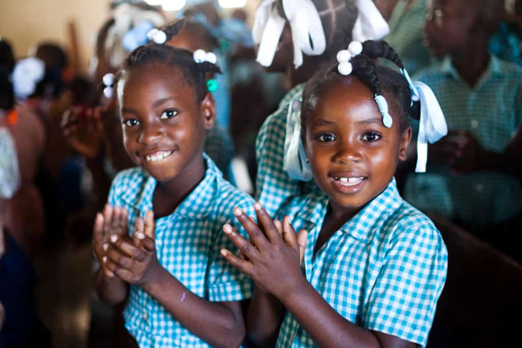 Two girls in blue and white smile and clap their hands during a program at the center.