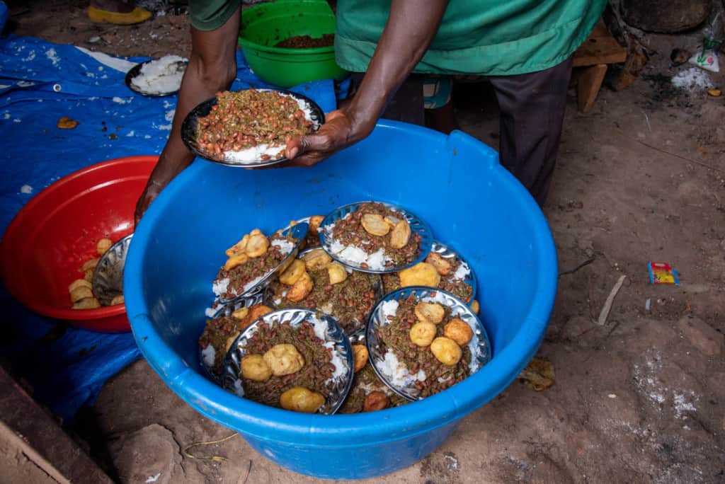 A social worker puts food onto plates before distributing it to the children. The food is rice and beans prepared with greens and Irish potatoes.