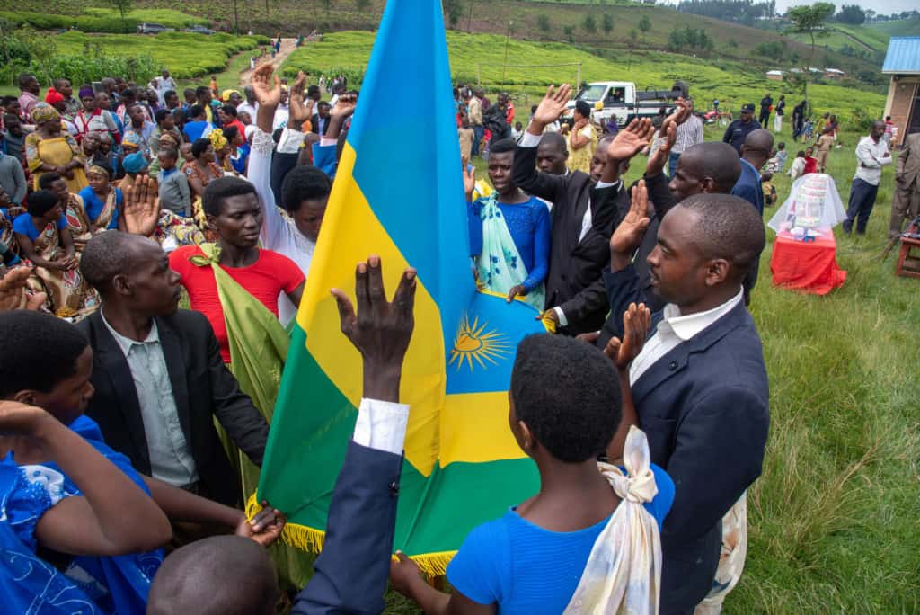 A group of men and women are holding the Rwandan flag on one hand and raising the other while making their vows during the marriage ceremony.