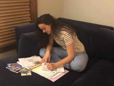 Katie writes to her sponsored child while sitting on her couch.