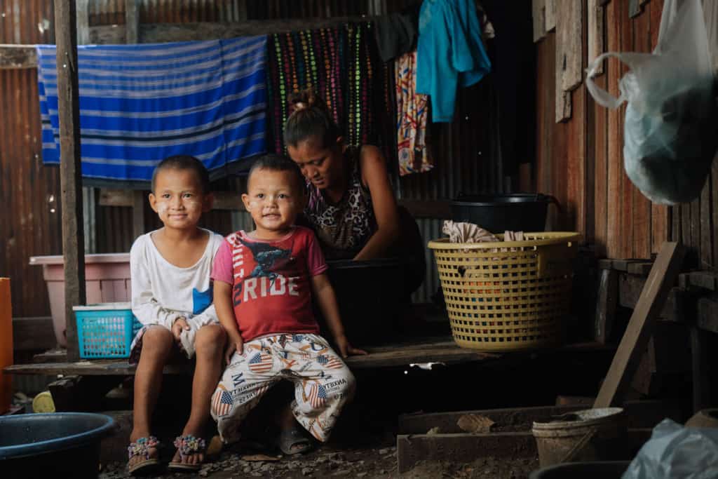 Two children at home sitting in front of their aunt while she is hand washing laundry.