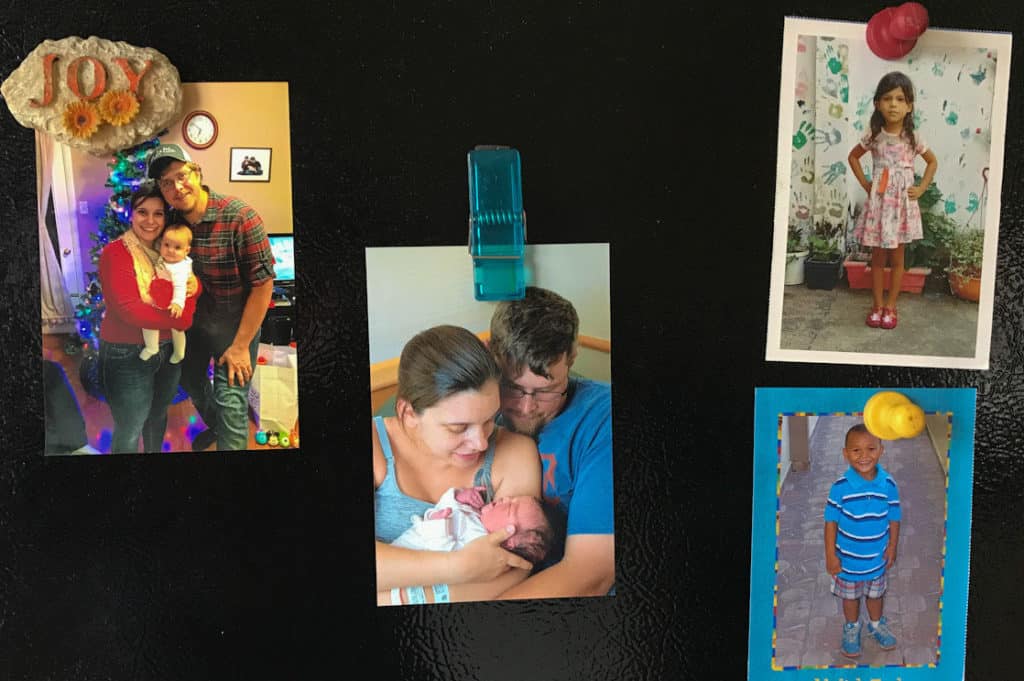 Sarah's black refrigerator door shows four family photos, including photos of the children the sponsors.