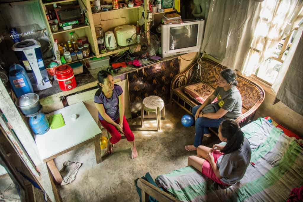 A mother and daughter are visited by a Compassion project director. They are sitting together in their small house.