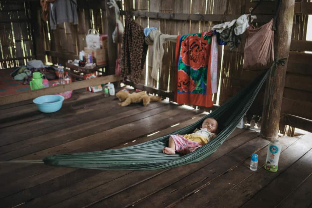 Toddler wearing a yellow shirt and pink shorts. She is sleeping in a green hammock in her home.