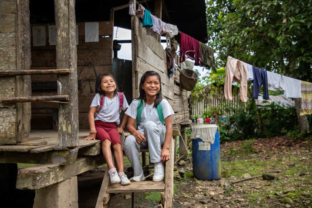 Two sisters outside of their home sitting on the stairs. There are clothes on a clothesline outside the house.