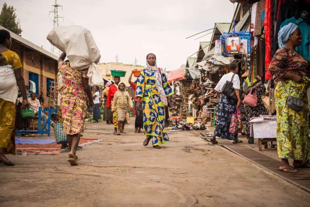 A woman walks through the marketplace in her local neighborhood. She is wearing colorful clothing. Many people are shopping and walking around her.