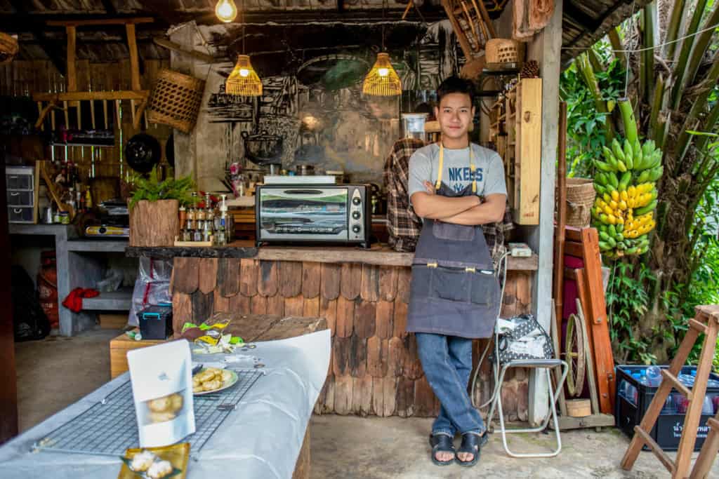 Young man standing in front of a counter at a cafe. The cookies he made are on the table for a presentation.