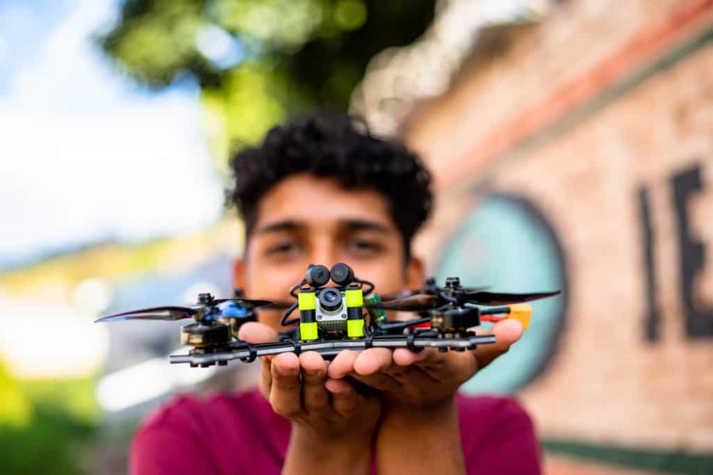 Miguel, in a red shirt, is outside the Compassion center holding the drone he learned to assemble through the center’s training. Miguel's face is out of focus.