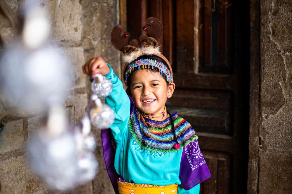 Girl at her home holding Christmas ornaments. She is wearing traditional clothes and a reindeer hat. 