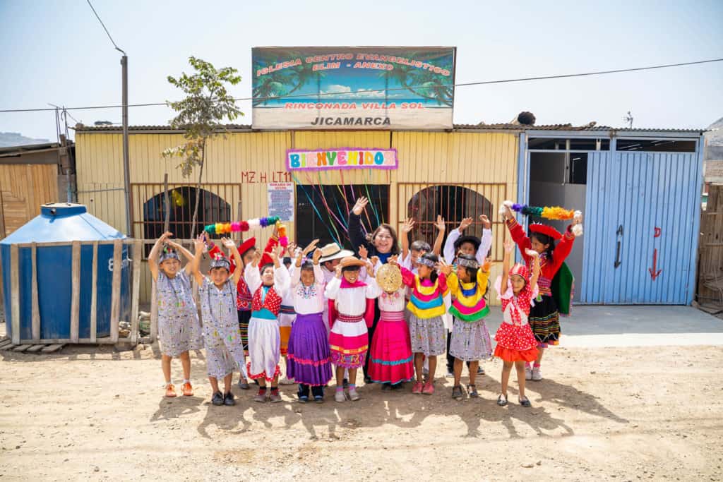 Compassion Peru's national director posing with children in front a church. The children are smiling and waving while wearing brightly colored clothing.