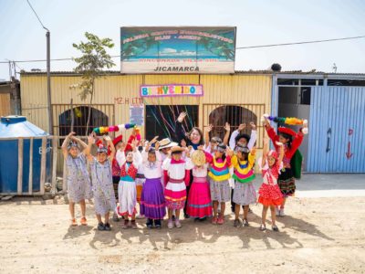 Compassion Peru's national director posting with children in front a church. The children are smiling and waving while wearing brightly colored clothing.