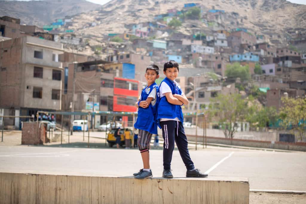 Two boys standing back-to-back with their arms crossed. An empty cement basketball court and apartment building are in the backgroud.