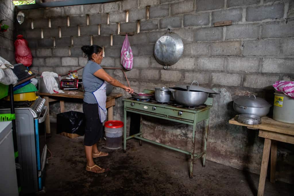 Woman wearing a grey shirt and a black skirt, and is preparing lunch for the Compassion beneficiaries. To help the kids gain weight, the nutritionist instructed the center to give them food that was high on protein and carbohydrates such as rice, beans, eggs and plantains. 