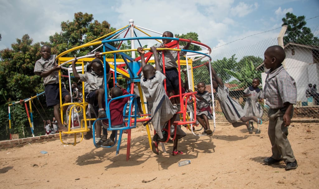 Children play outside on the sand, on a colorful playground, swings, merry-go-round, laughing, playing. 