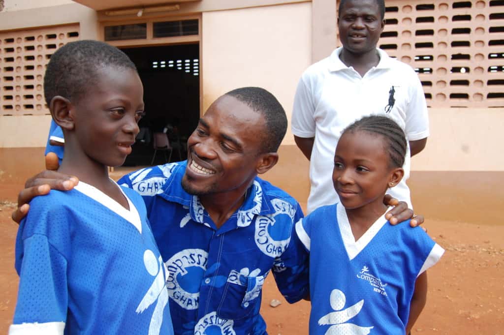 A Compassion center worker in Ghana engages with two young children. They are all wearing blue Compassion logo shirts