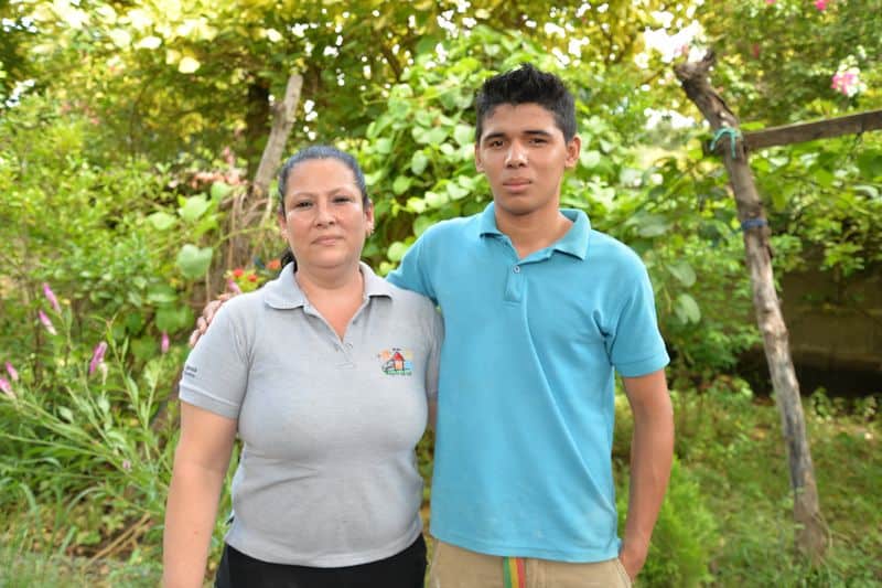 A teenage boy wearing a blue polo shirt stands with his arm around his Compassion center tutor, a woman wearing a gray polo shirt