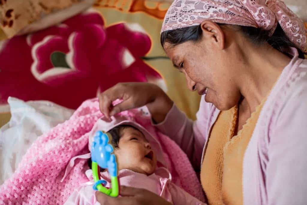 Woman holding her baby who is wearing pink. They are playing with a rattle.