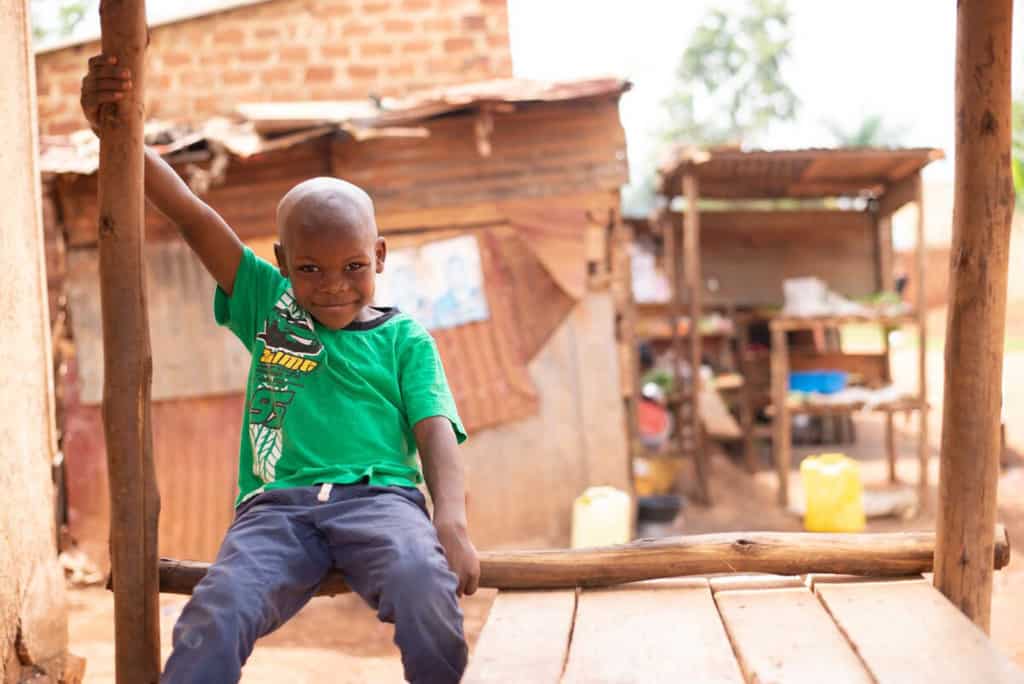 Boy sitting on the front porch and is wearing a green shirt and blue pants.