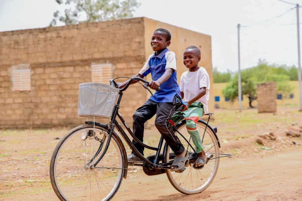 Two boys ride on a bicycle down a dirt road in Burkina Faso.