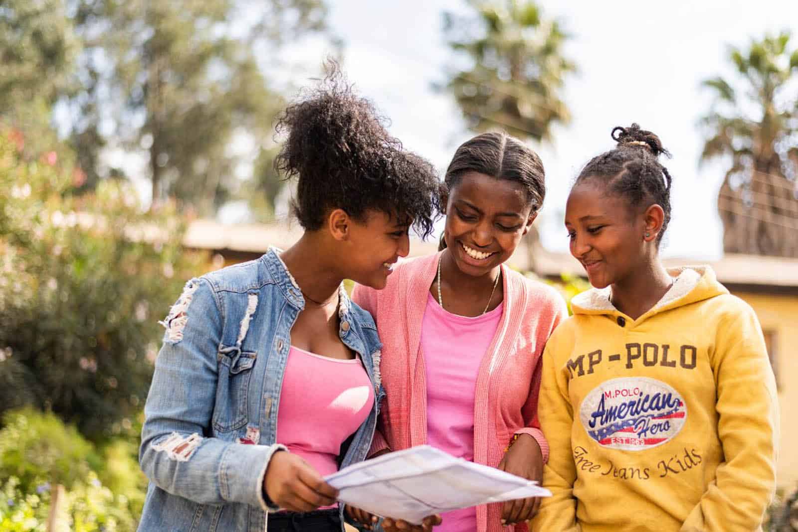 Three teenage girls smile as one of them holds a letter from her Compassion sponsor.