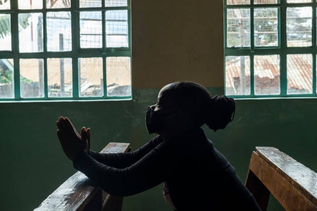 A girl in Kenya sits in a church pew praying. 