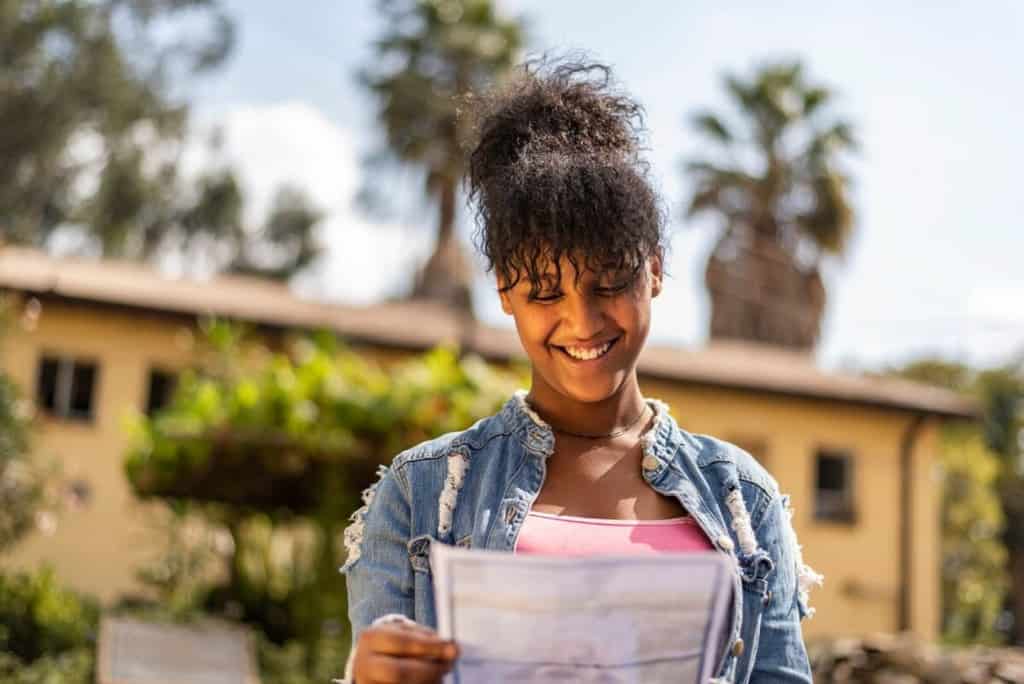 Mekdelawit is wearing a pink shirt and a jean jacket. She is outside and is holding a letter she is writing to her sponsor.