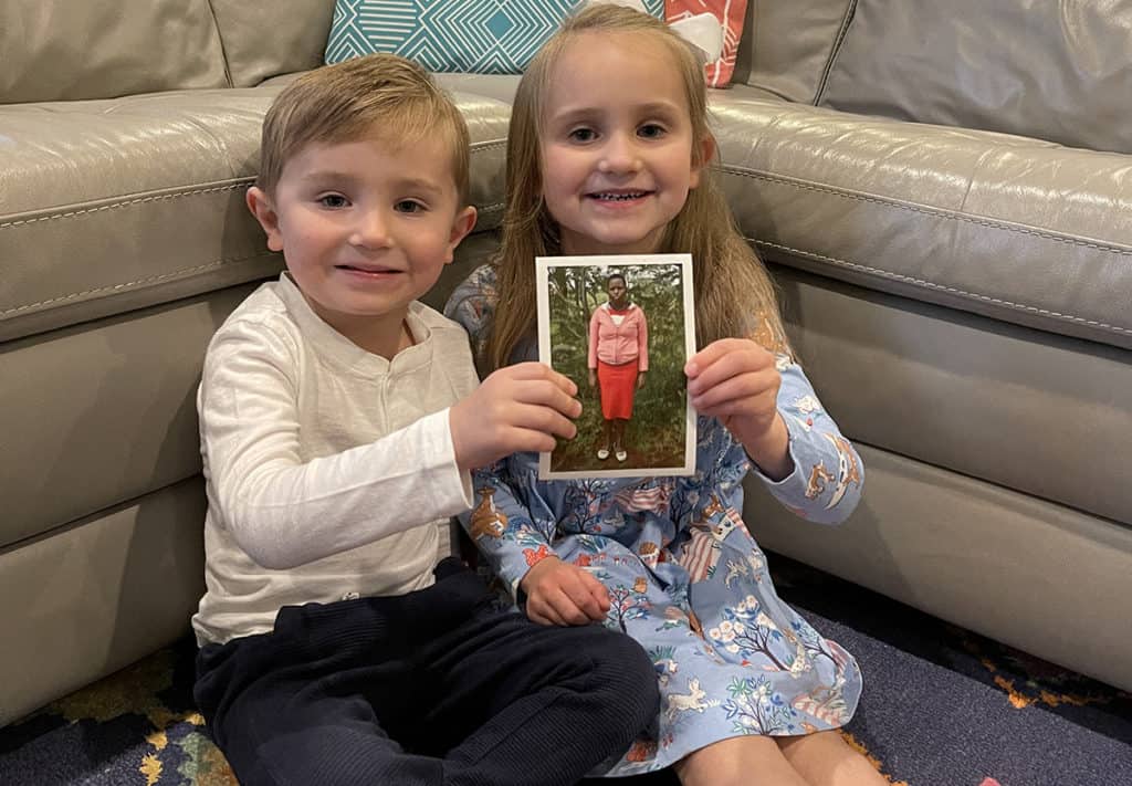 Two young children are smiling and holding a photo of the youth their family sponsors through Compassion. 