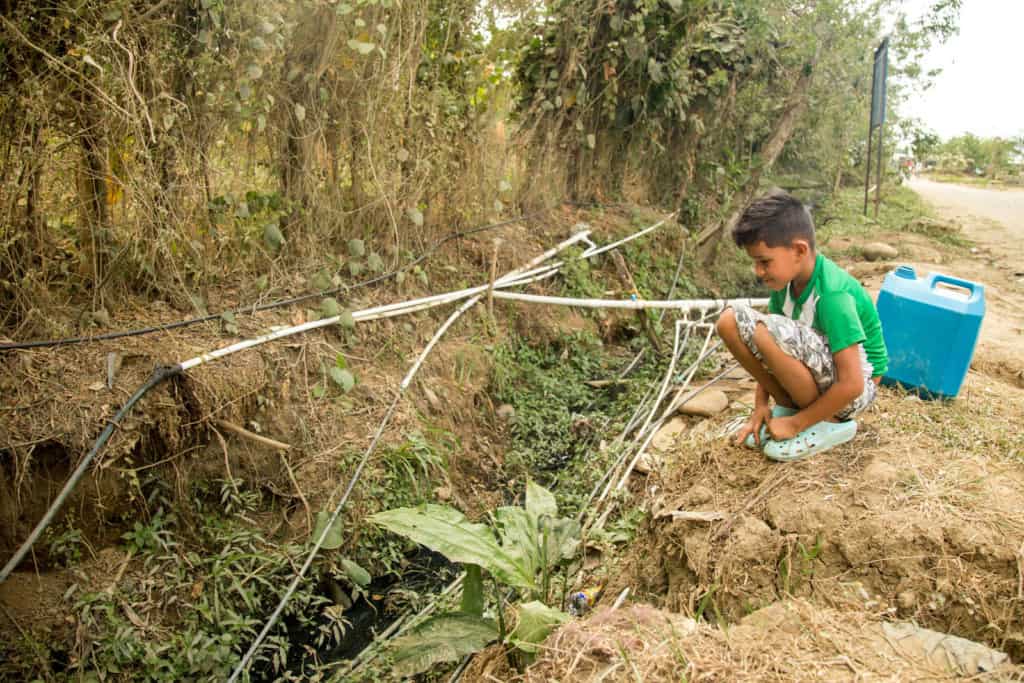 Boy seated next to one of the hoses connections people in his community use to distribute water.