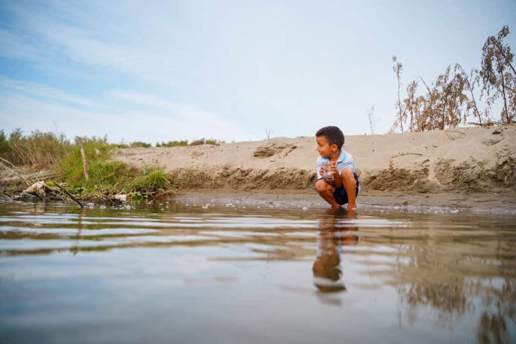 A child is kneeling down beside a river that runs in the Tamarindo community.