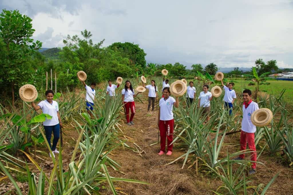 A group of gardeners stand in a garden in Colombia holding their straw hats and smiling